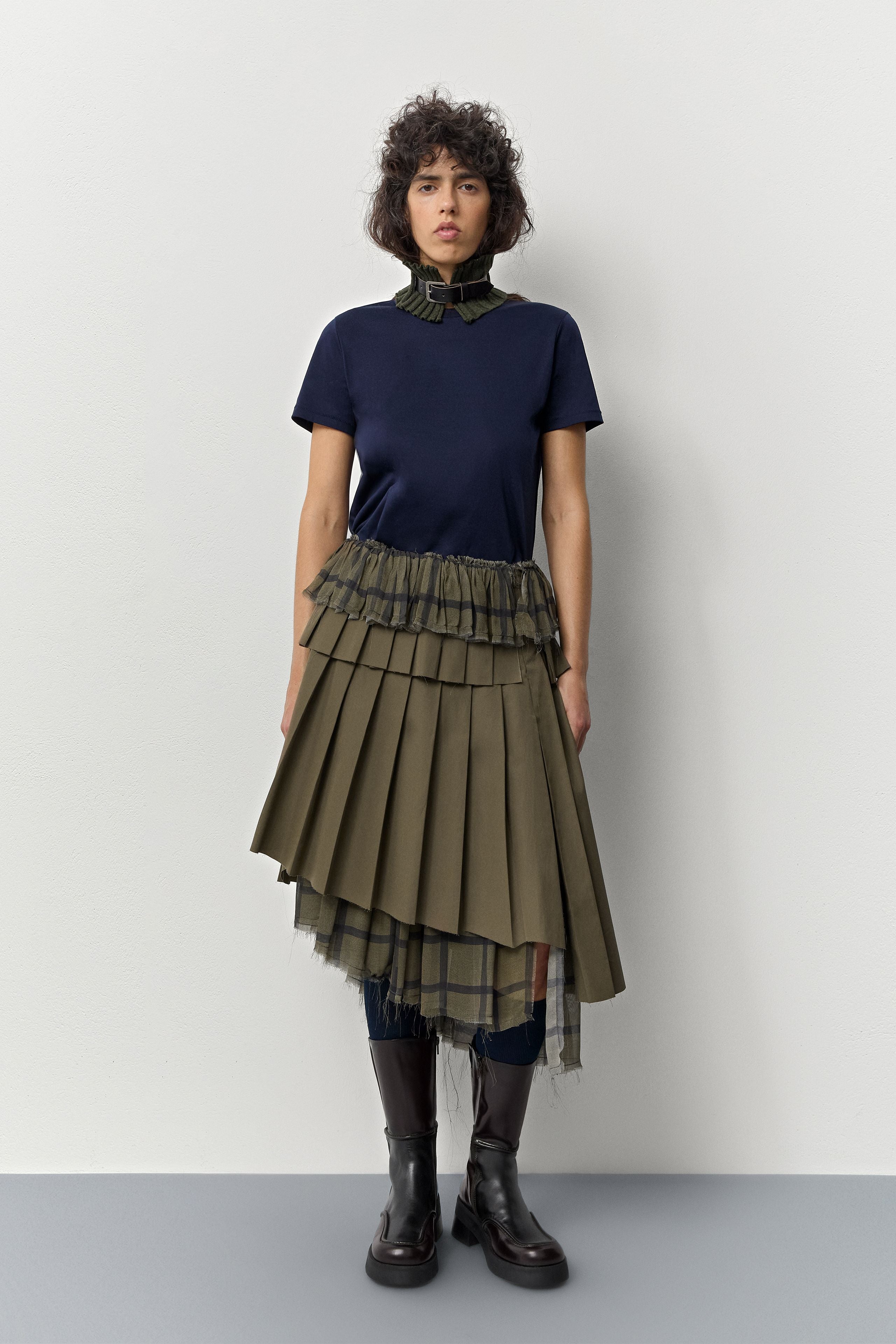 Woman wearing a navy top and green pleated skirt with brown Miista Inne boots against a white background