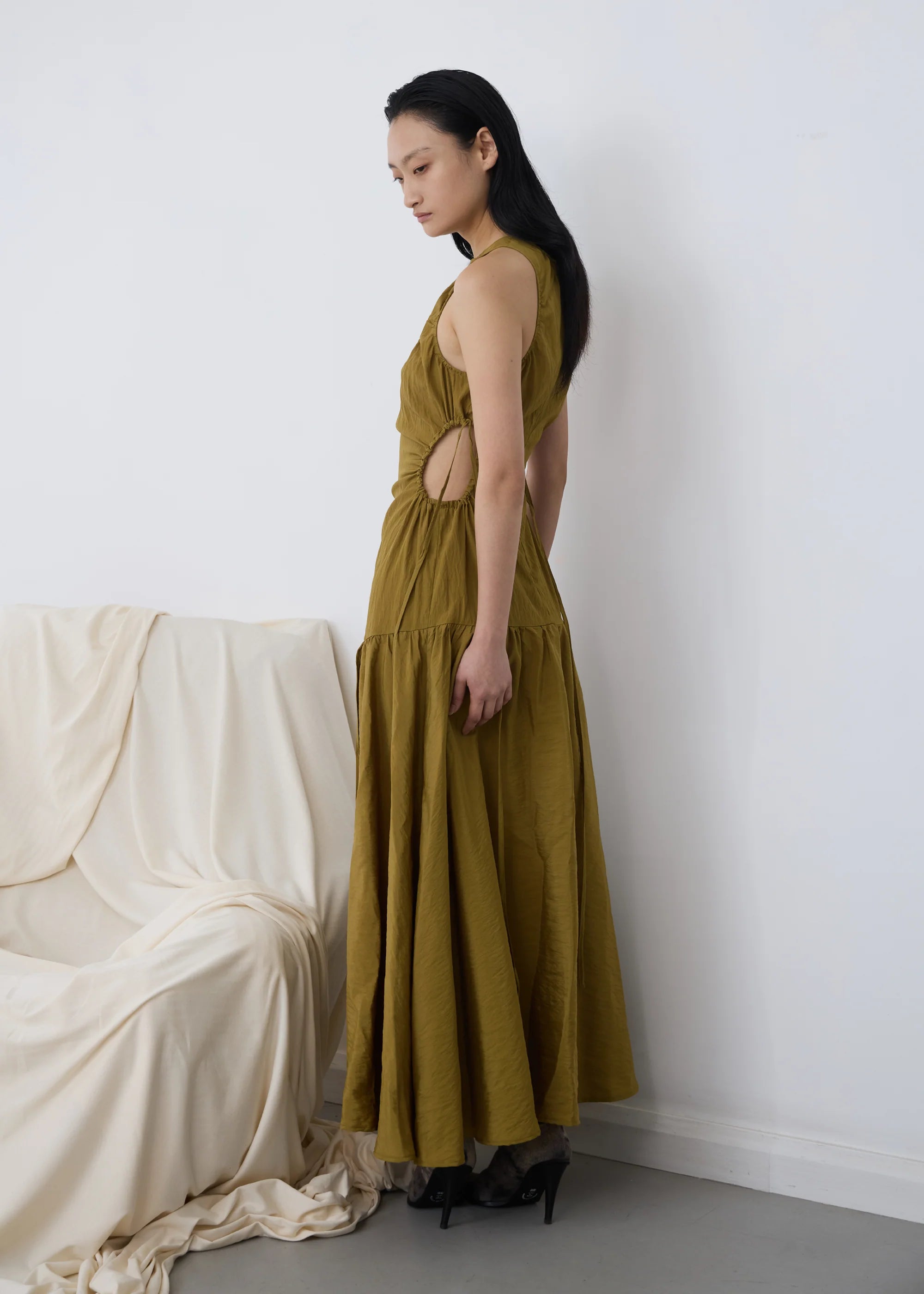 Woman wearing a long kelp orbit PV dress with cut-out details, standing against a white wall.