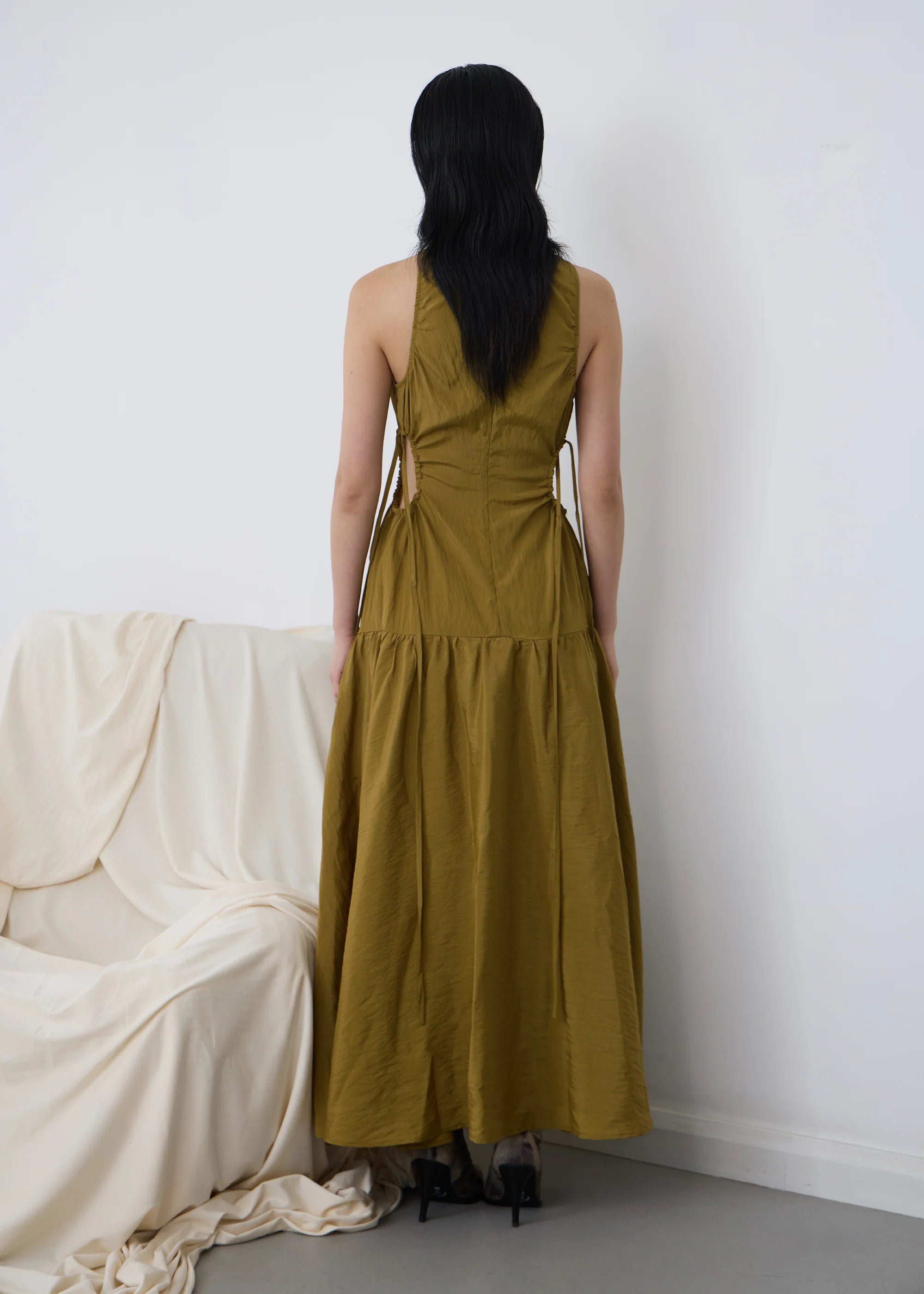 Woman wearing a long kelp orbit PV dress standing in front of a white wall with a beige curtain.