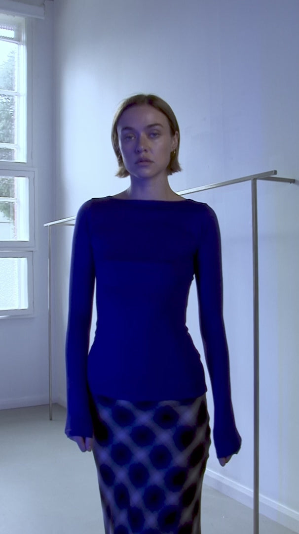 Video of Woman wearing permanent vacation ultra marine connection top and check skirt against a white wall