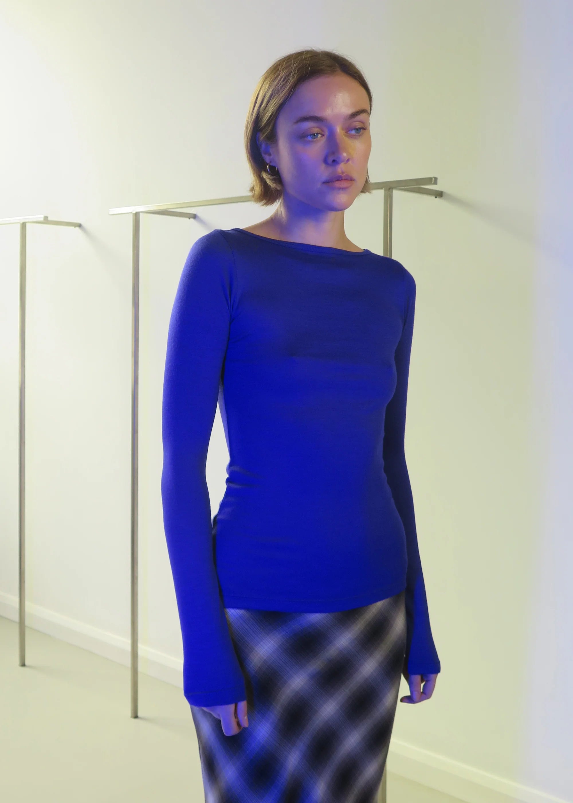 Woman wearing permanent vacation ultra marine connection top and check skirt against a white wall 
